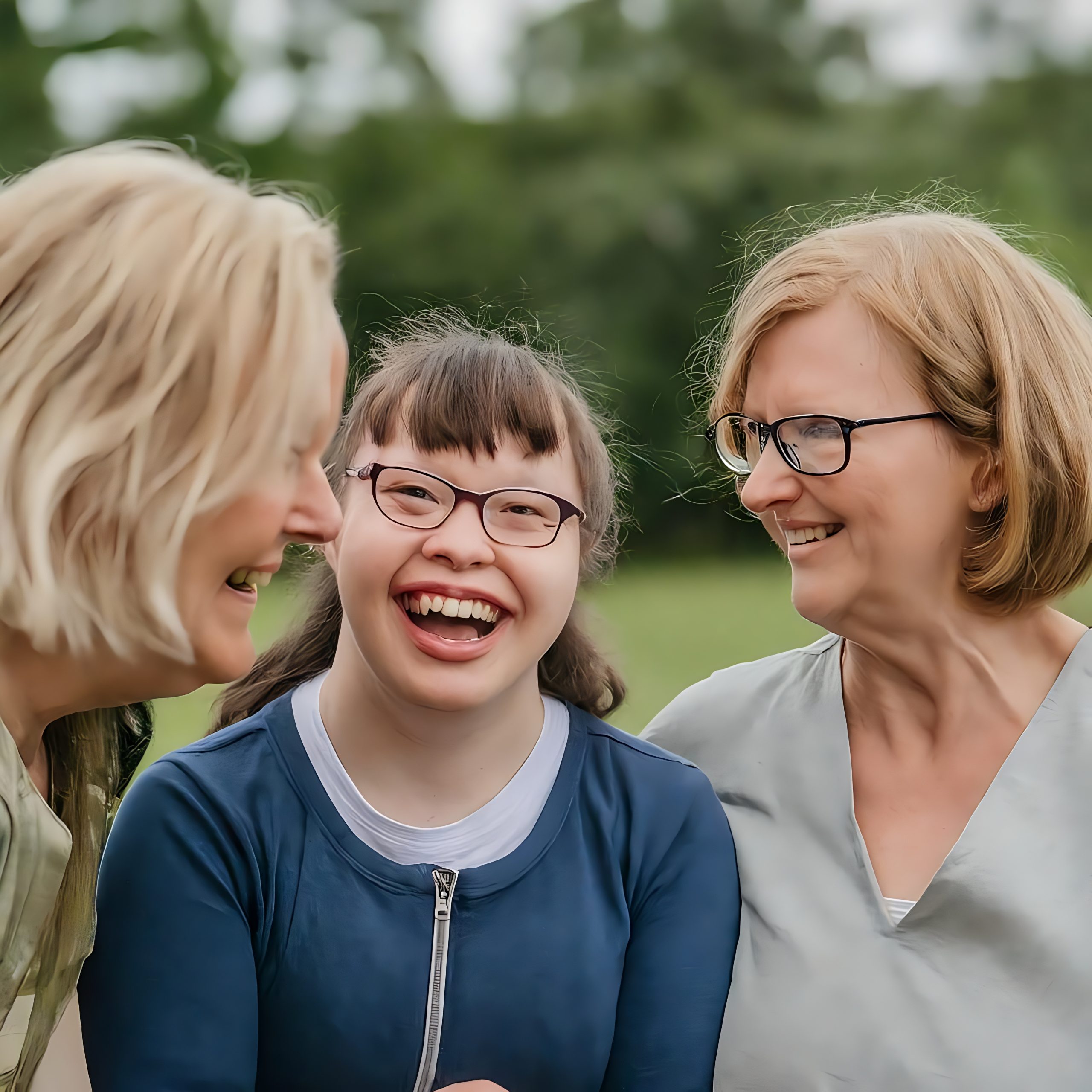 Groupe de femmes sourriantes, avec une personne autiste au centre, dans un milieu naturel.