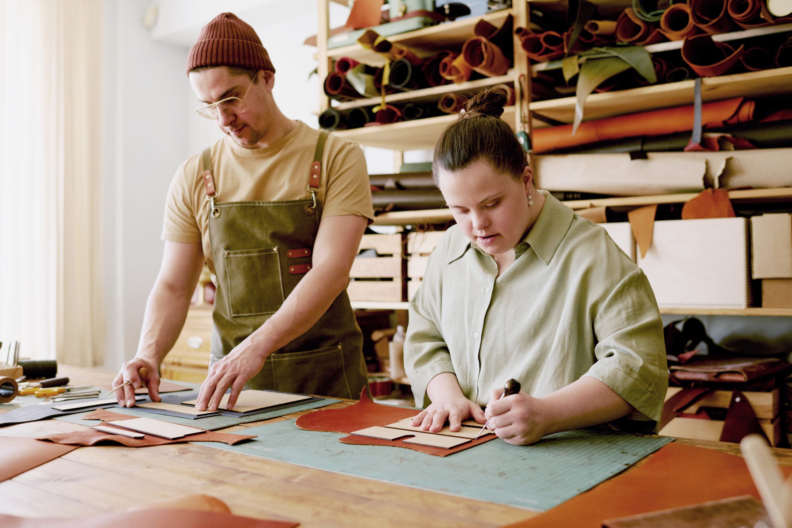 Tailleur homme et sa collègue femme avec la trisomie des détails en cuir au travail atelier antique équipé d'outils de couture et de tissus