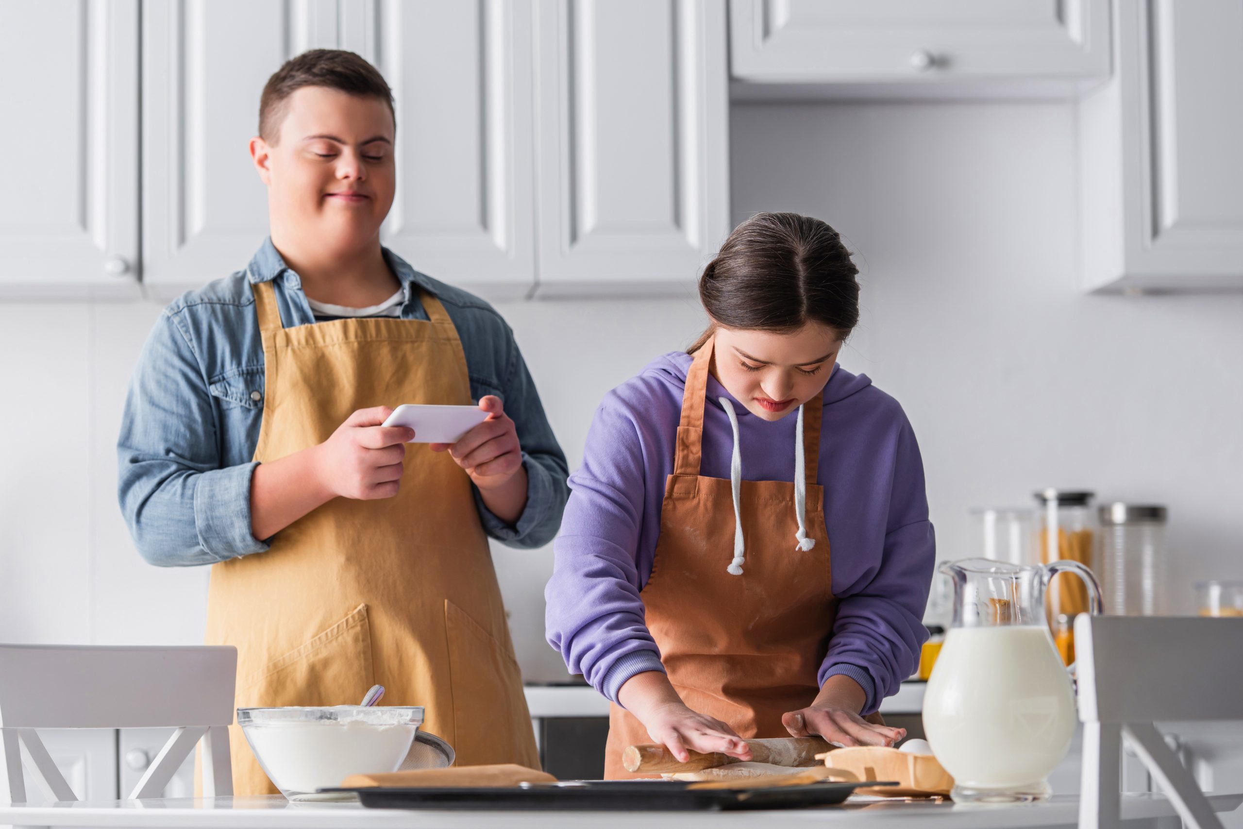 Jeune adulte autsite faisant de la pâte avec une amie et en tenant un smartphone en cuisine